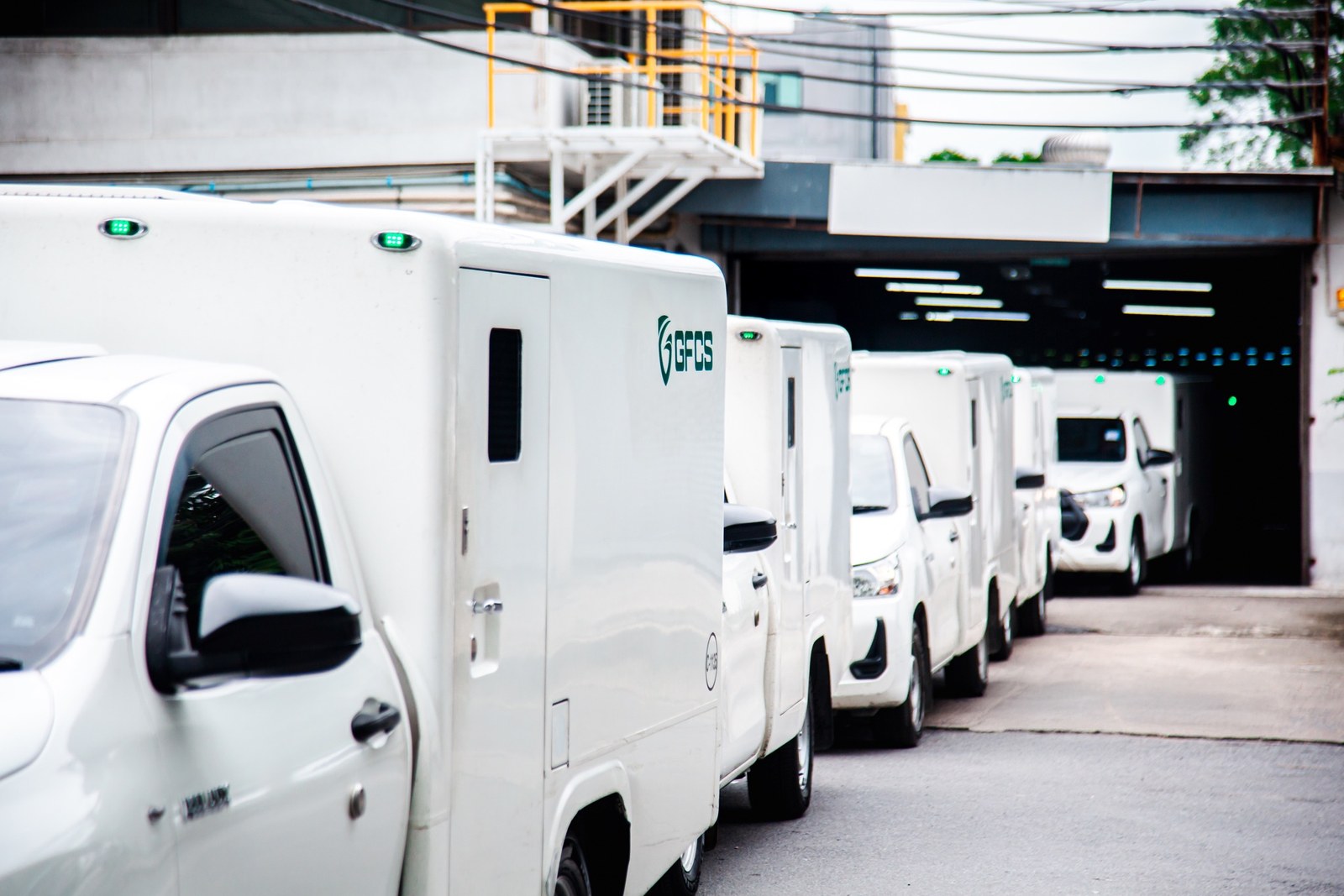 A line of white GFCS armoured cash-in-transit pickups parked outside a cash centre loading bay.